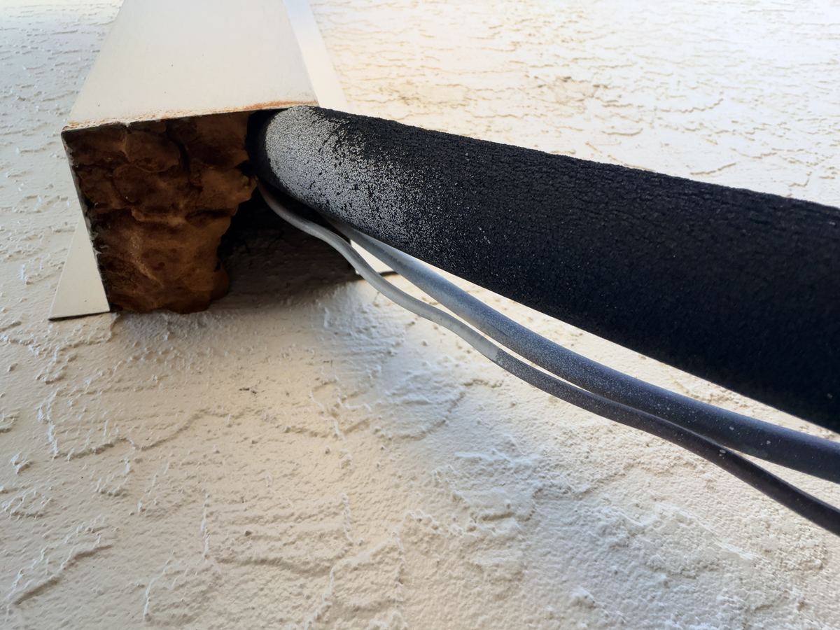 An AC line set and wires entering a wall through a cover that has been packed with crumbling foam.