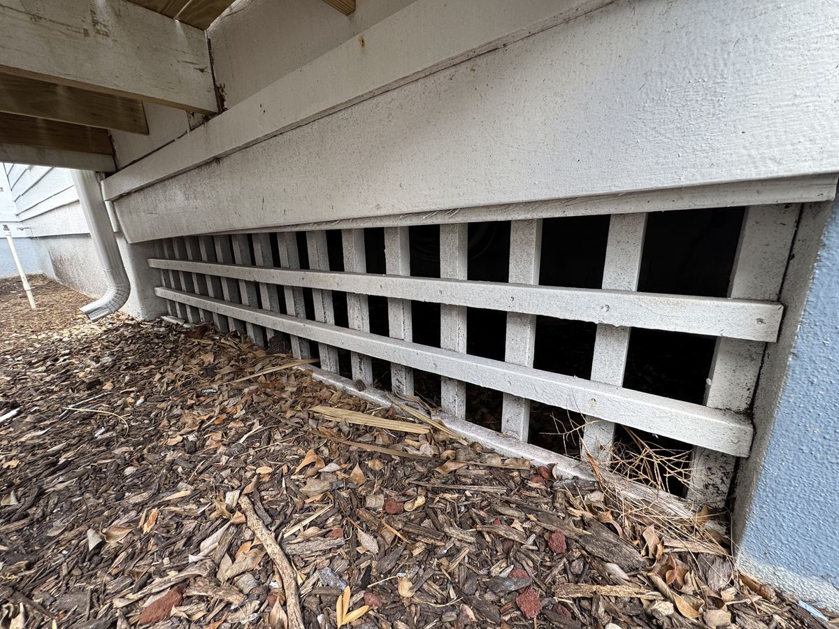 Wooden lattice skirting along the base of a raised home, with wide openings into the dark crawlspace behind it.