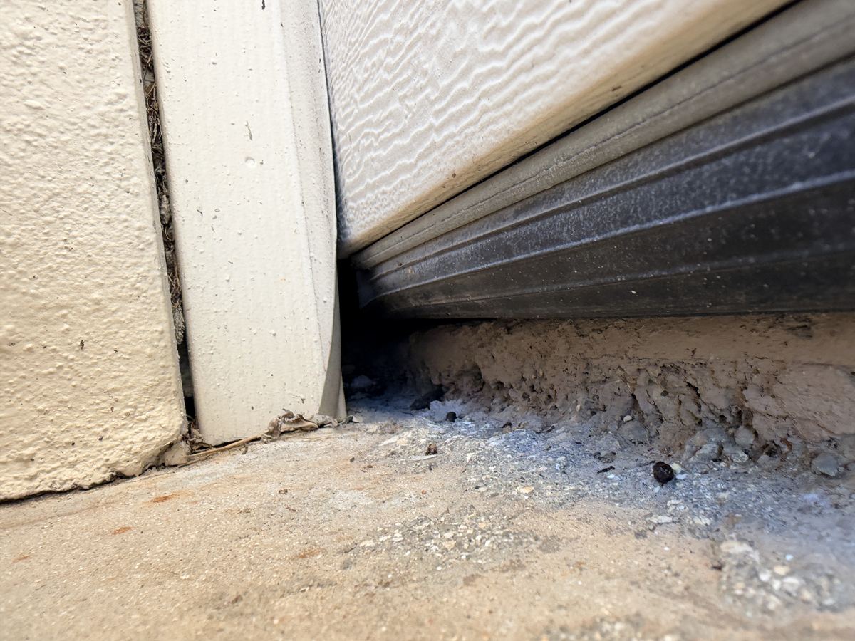 The bottom corner of a garage door, where the seal stops short and droppings have collected in the open gap.